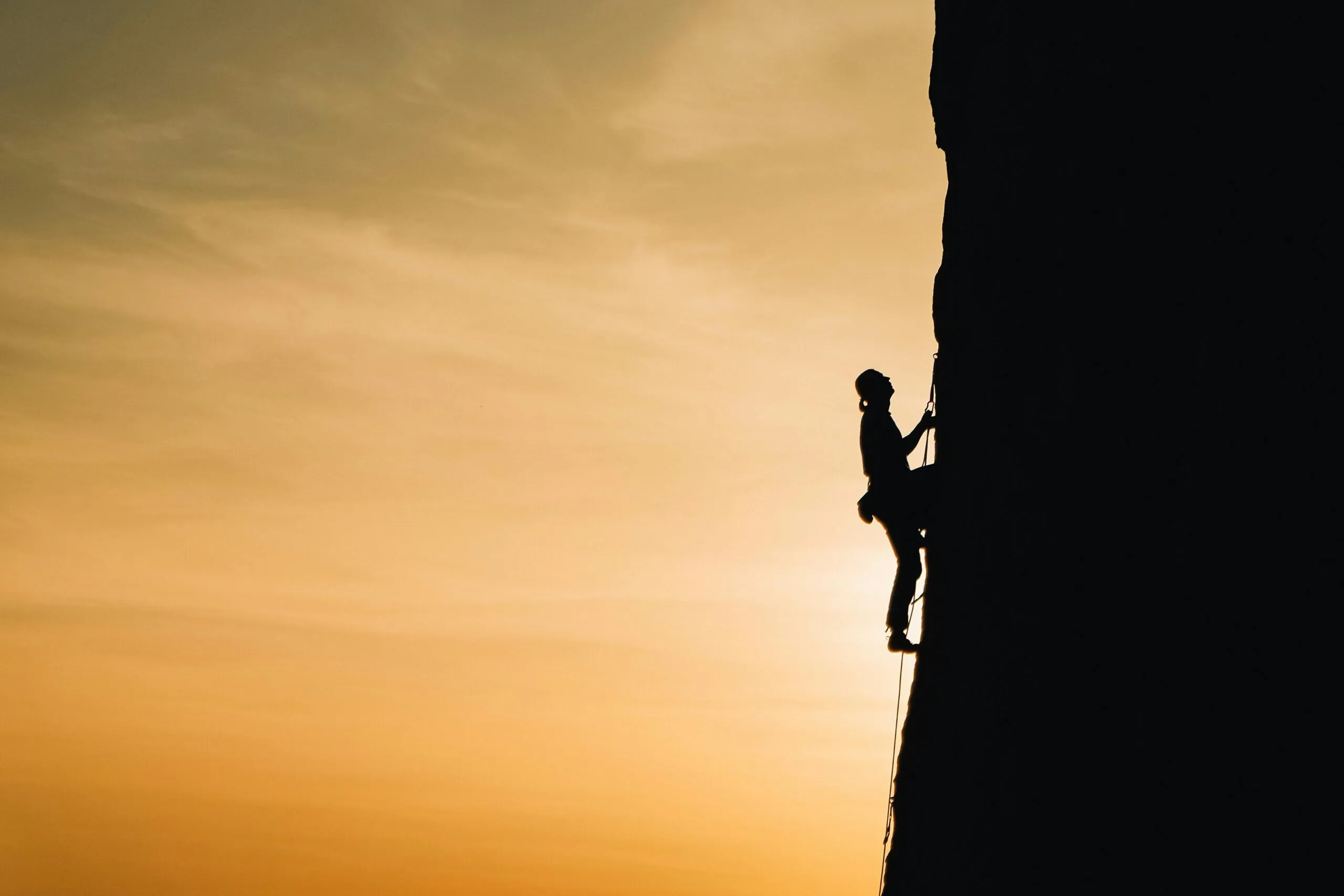 Rock climber scaling a cliff at sunset representing perseverance and the recovery journey from sexually compulsive behavior