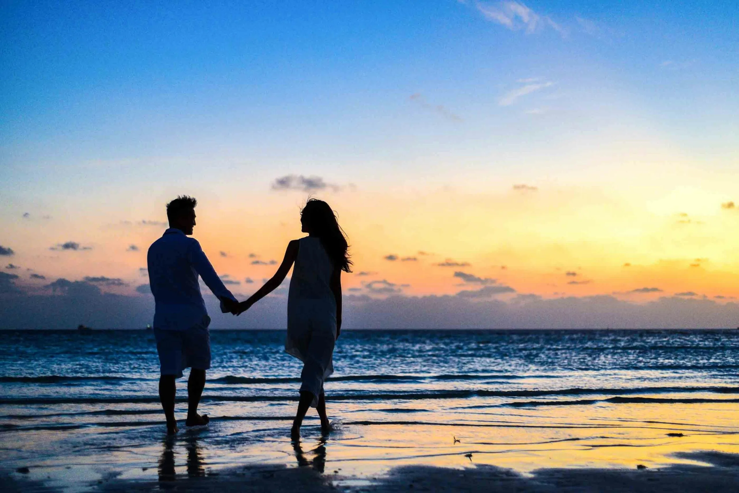 Couple walking hand in hand on a beach at sunset representing healing and renewed connection in infidelity recovery