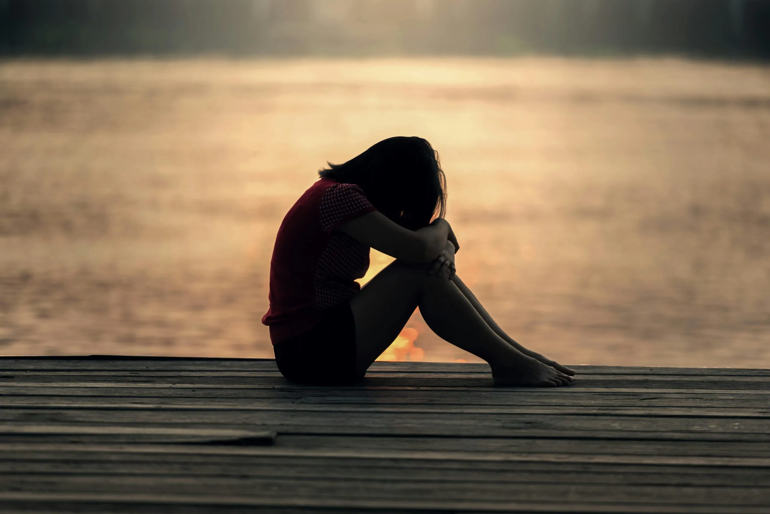 Woman sitting alone on a dock by a lake representing solitude, grief, and healing after infidelity