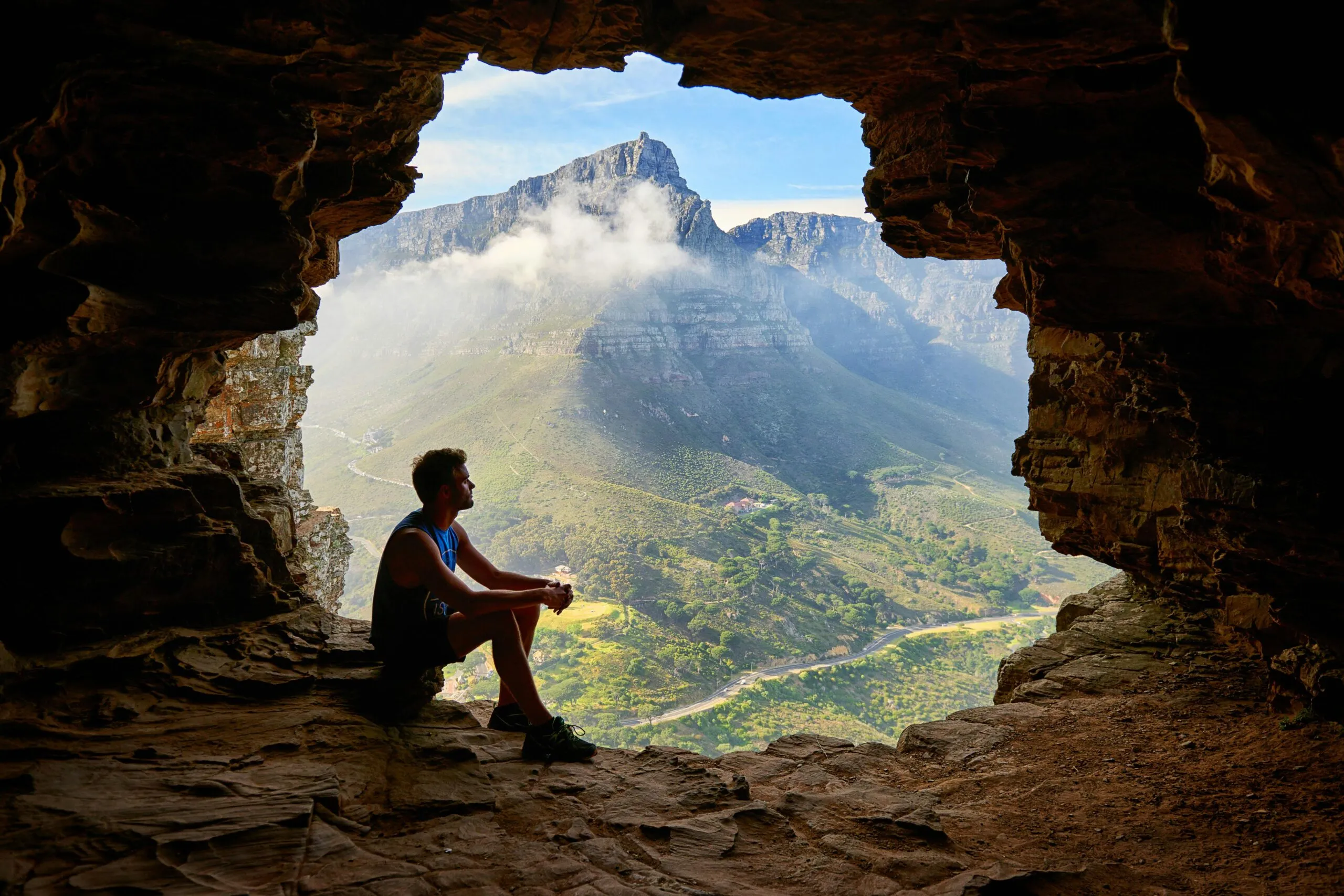 Man sitting in a cave overlooking a mountain landscape representing self-reflection and perspective in sexually compulsive behavior recovery