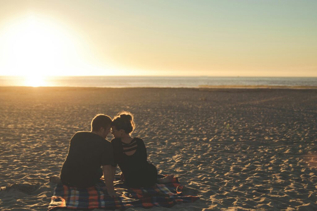 A couple enjoys sunset together on a sandy beach, capturing a moment of love and togetherness.