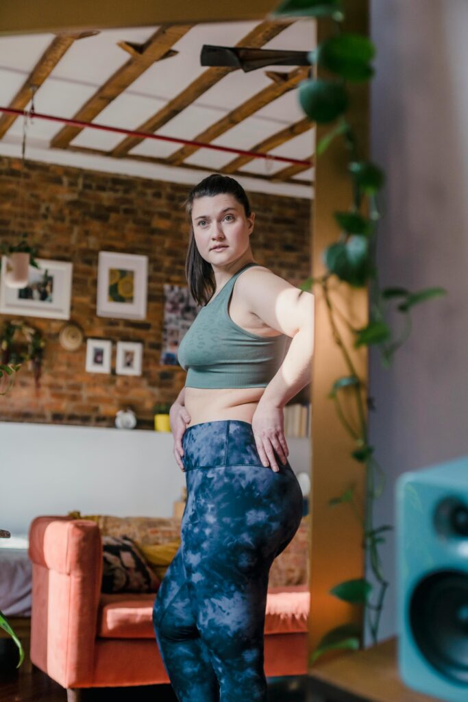Woman in activewear checks reflection in mirror inside cozy room with modern decor.