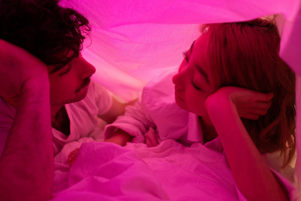 Close-up of a couple sharing intimate moment under pink-lit blanket.