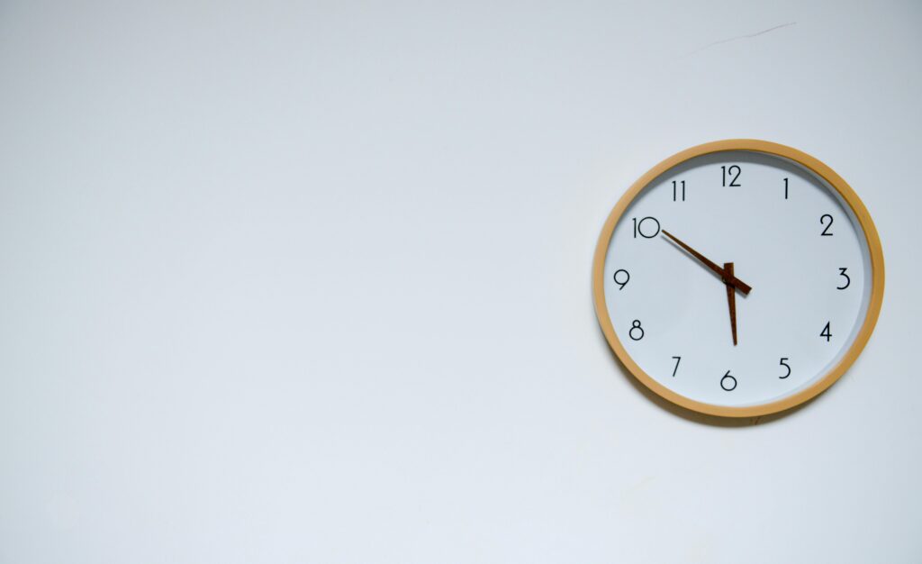 Simple wall clock with wooden frame against a white background, showing the time 10:10.