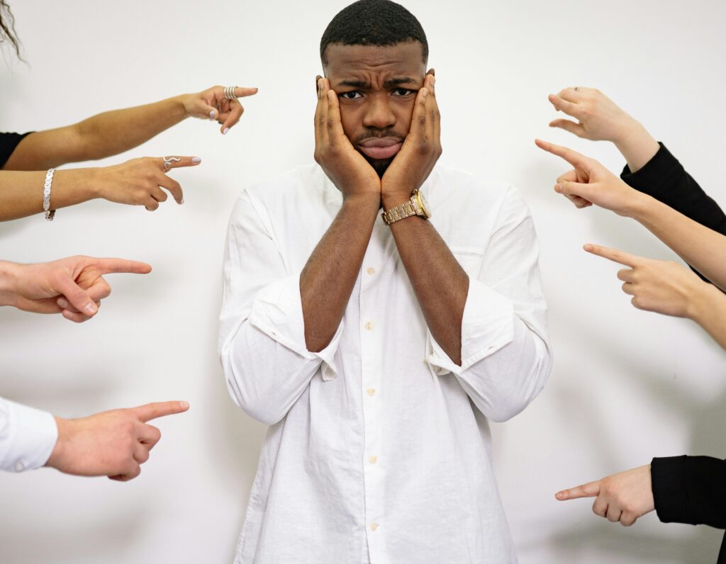 Worried man surrounded by pointing fingers, symbolizing bullying and social pressure.