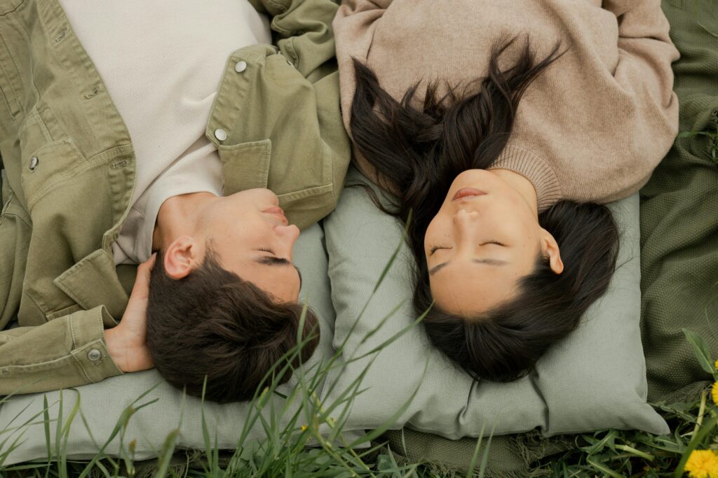 A couple lying side by side on grass, eyes closed, enjoying a peaceful moment outdoors.