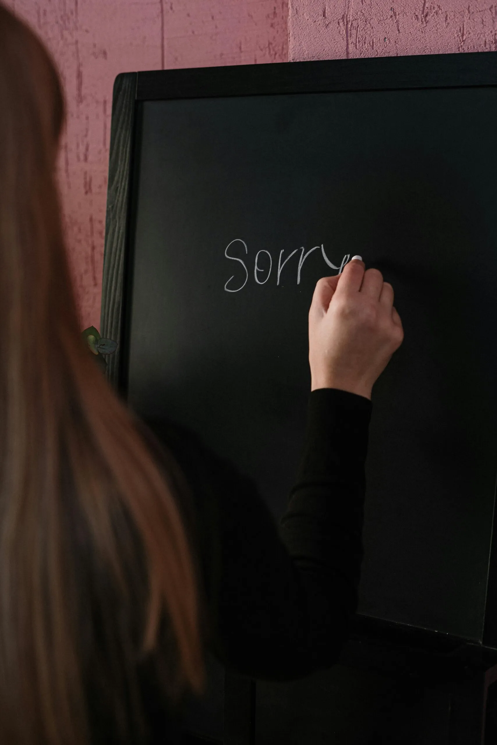 Person writing sorry on a blackboard representing the need for an effective apology in relationships