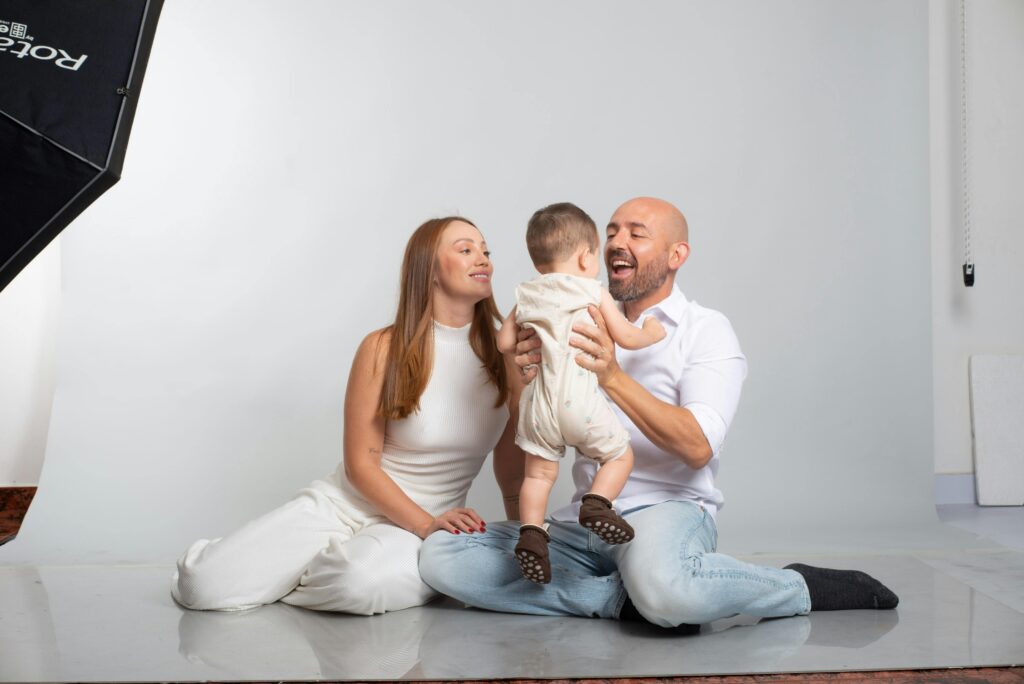 A joyful family moment captured with parents and baby in a bright photography studio setting.