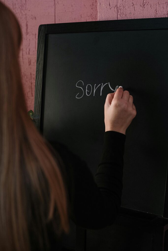 Side view of a person writing 'Sorry' on a blackboard indoors, conveying an apology.