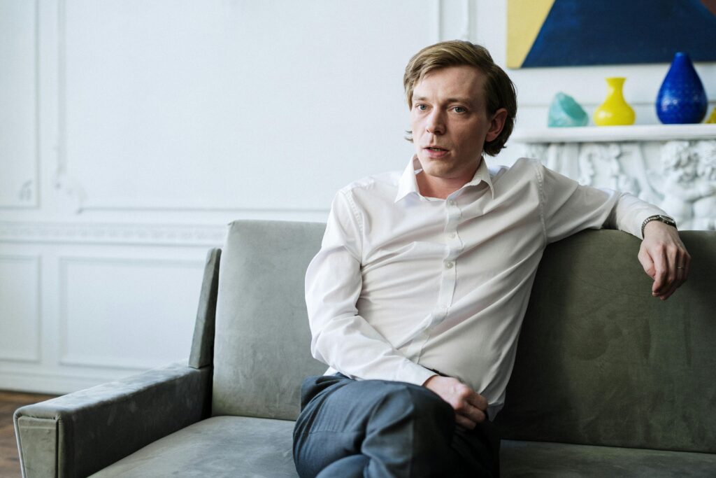 Confident man in white shirt sitting on sofa, representing consulting or therapy session indoors.