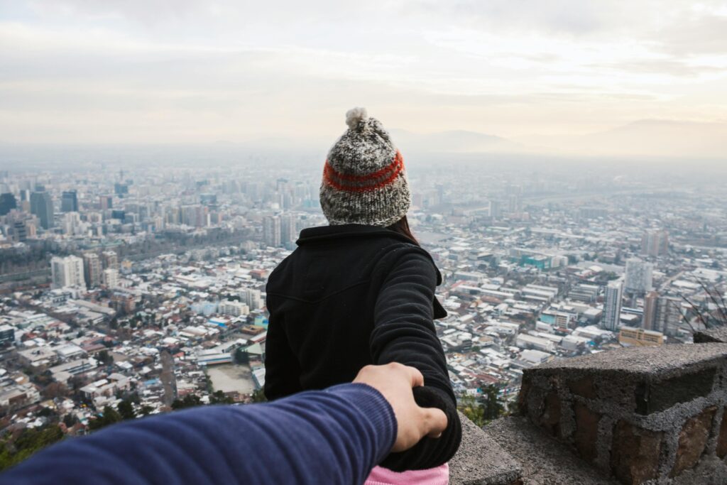 A couple holding hands overlooking a vast urban cityscape, emphasizing travel and togetherness.