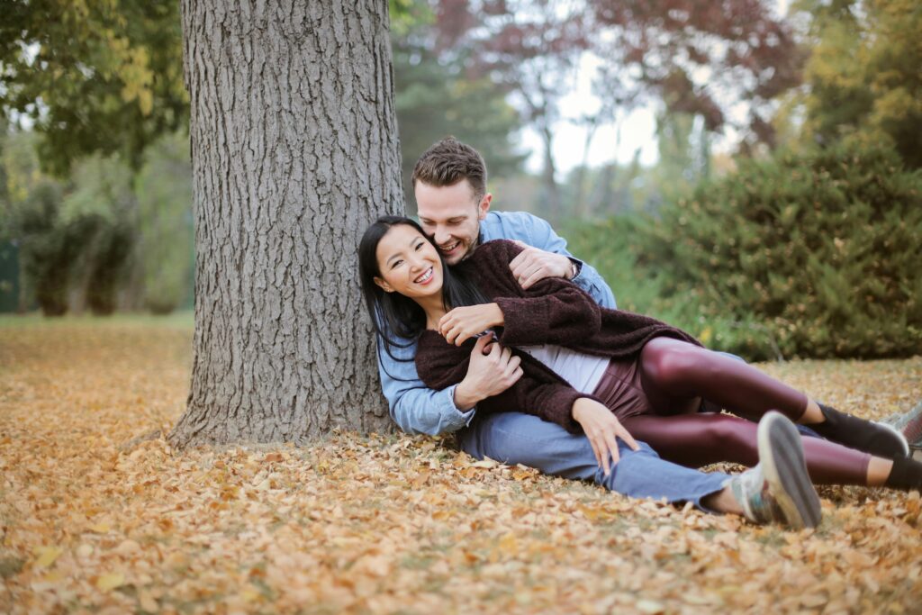 Romantic couple enjoying a playful embrace under a tree during fall.
