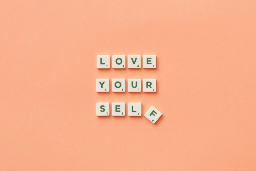 Scrabble tiles spelling 'Love Yourself' on a peach background, inspiring self-care.