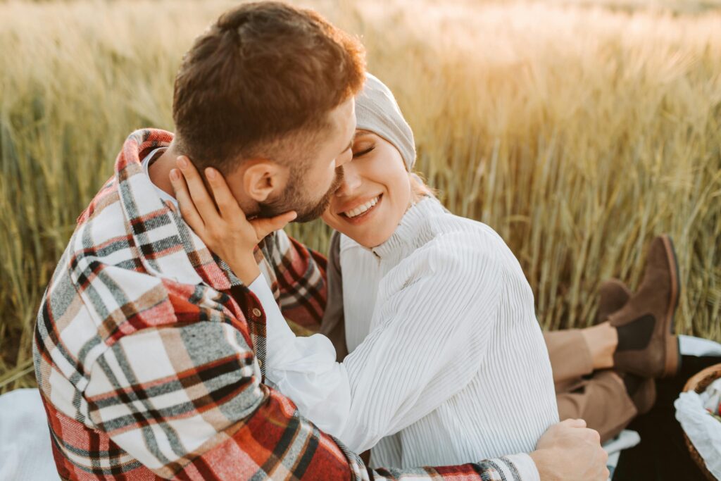 Happy couple embracing in a wheat field during sunset, enjoying a romantic moment together.